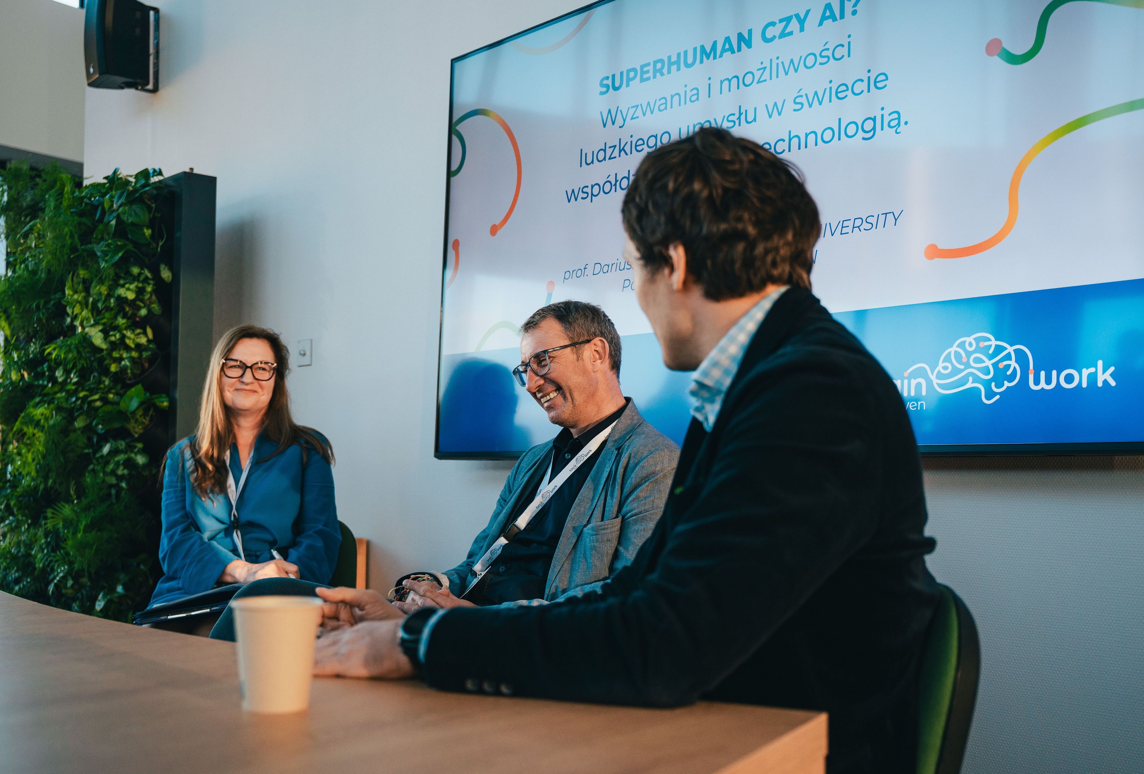 Panel dyskusyjny Brain-driven Work „Superhuman czy AI? Wyzwania i możliwości ludzkiego umysłu w świecie współdziałania z technologią”, trzy osoby rozmawiają przy stole w swobodnej atmosferze